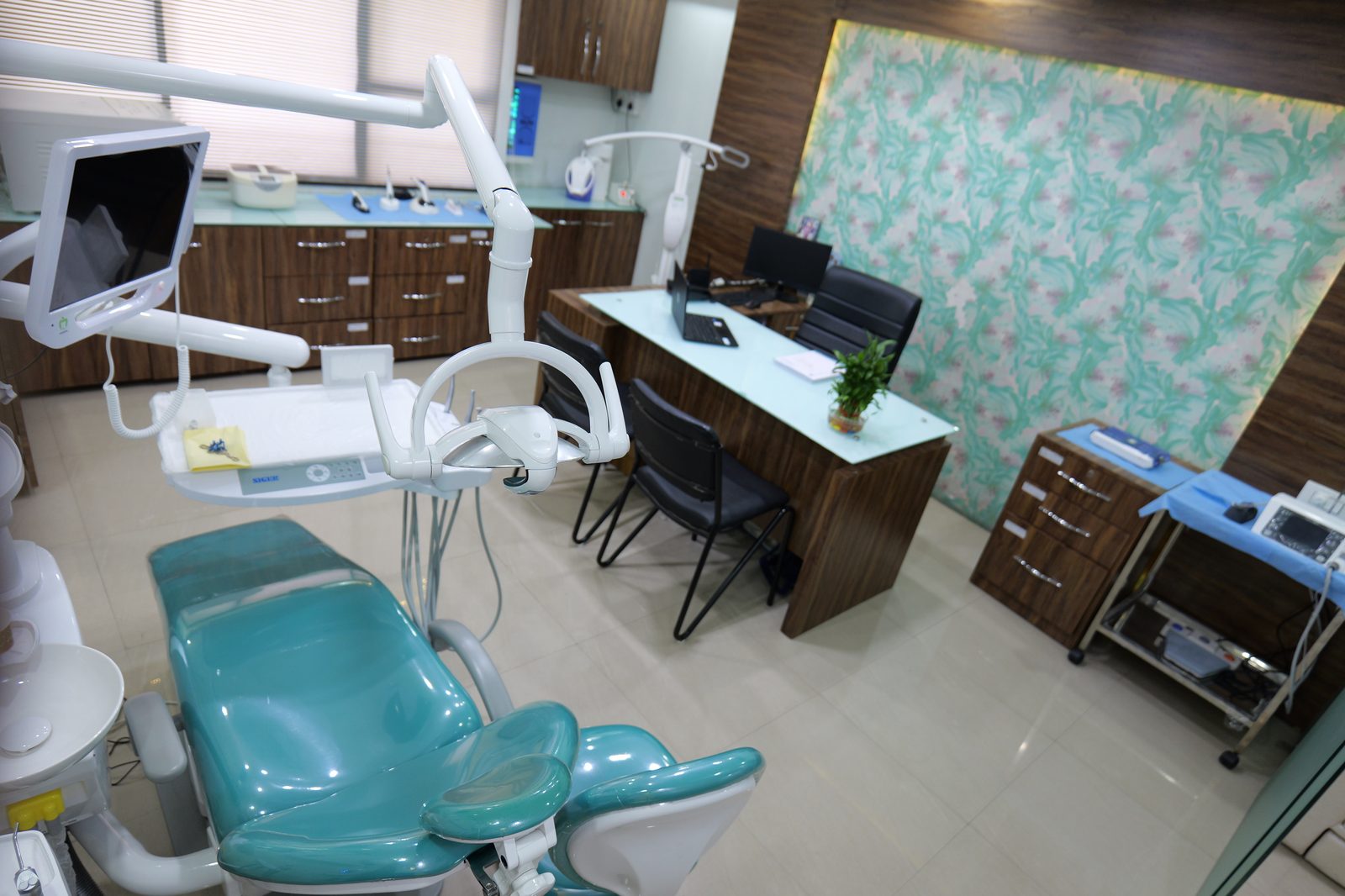 A treatment room at Shivaay Dental Clinic with a teal dental chair